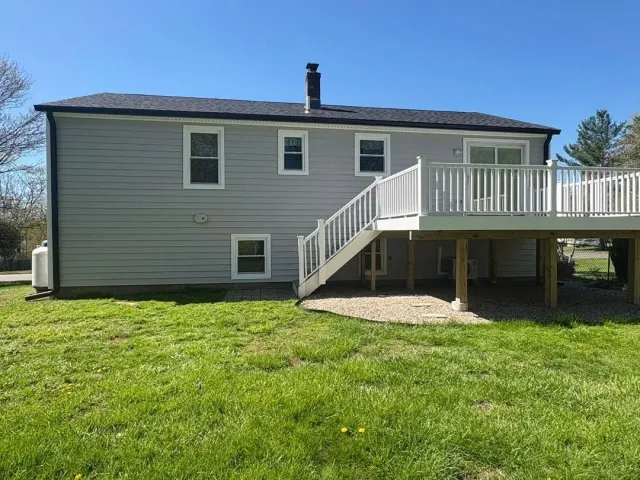 Gray house with white deck stairs and railing over a green lawn under a blue sky