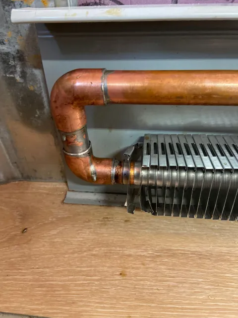 Copper pipe connected to a finned metal radiator, mounted on a wooden base.