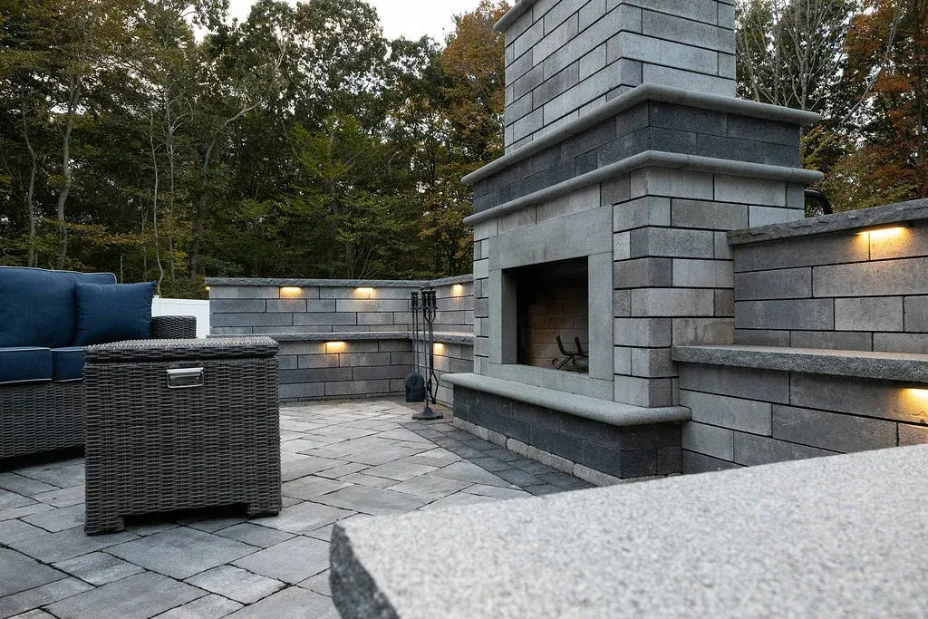 Outdoor stone fireplace with seating wall featuring built-in lighting in Easton, Massachusetts