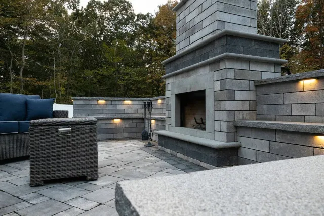 Outdoor stone fireplace with seating wall featuring built-in lighting in Easton, Massachusetts