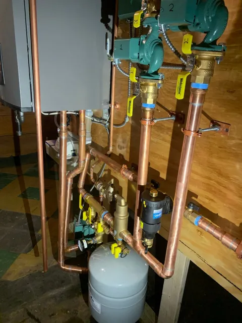 Copper pipes and boiler system components on a wooden wall.