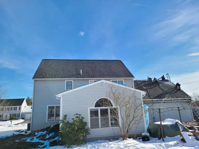 Two-story house with light blue siding, snow on the ground, and a clear blue sky.