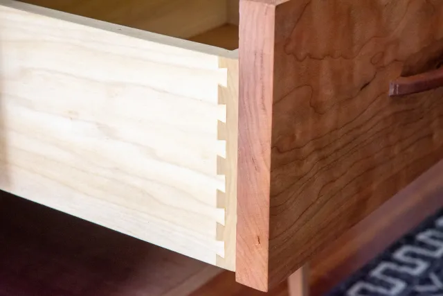 Close-up of two interlocking pieces of wood, one light-colored and one darker, with finger joints.