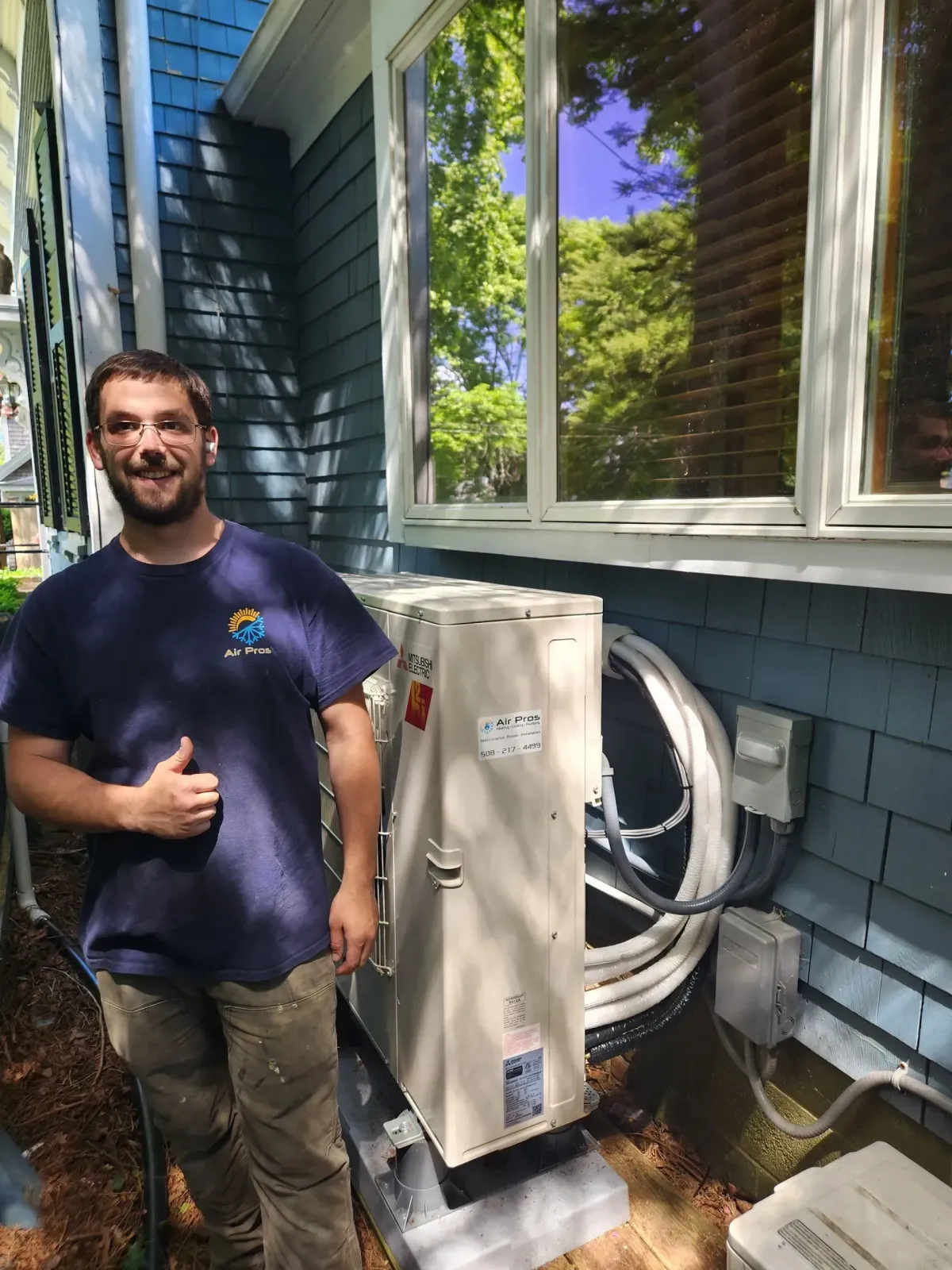 Man gives thumbs up beside new HVAC unit installed next to a blue house.