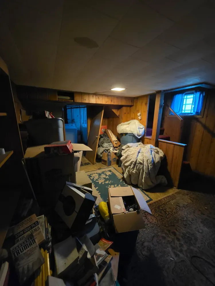 A cluttered wood-paneled basement before a Pioneer Valley Junk Removal cleanout