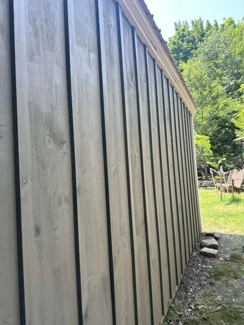 The side of a wooden building with a fence in the background.