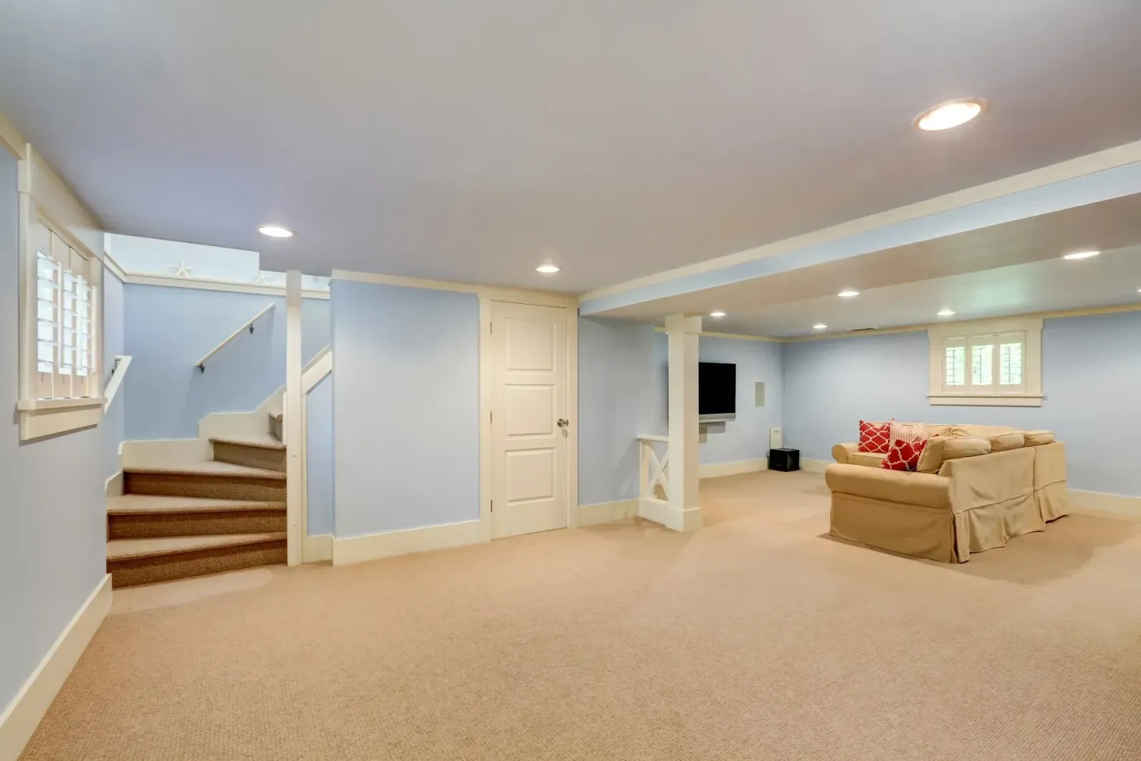 Basement living space with staircase, light blue walls, tan carpet, and a beige sofa.