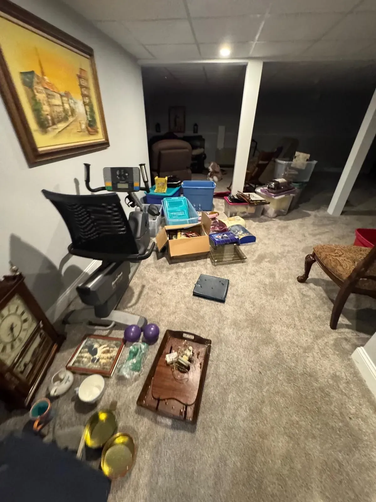 Cluttered basement with boxes, chairs, bins, and stored household items under exposed beams.