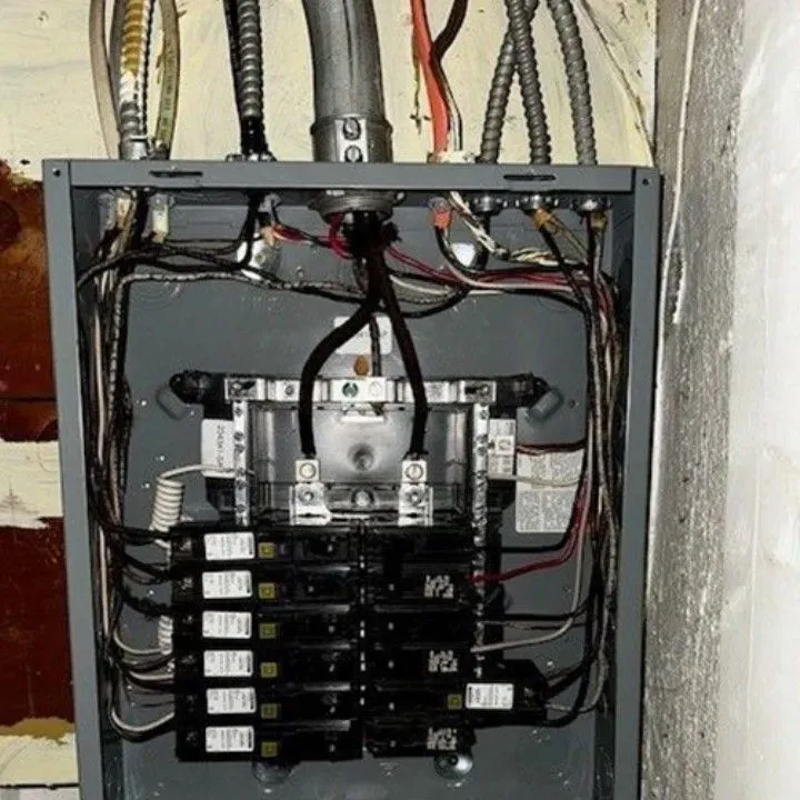 Electrical panel with wires and circuit breakers. Gray metal box mounted on a wall.