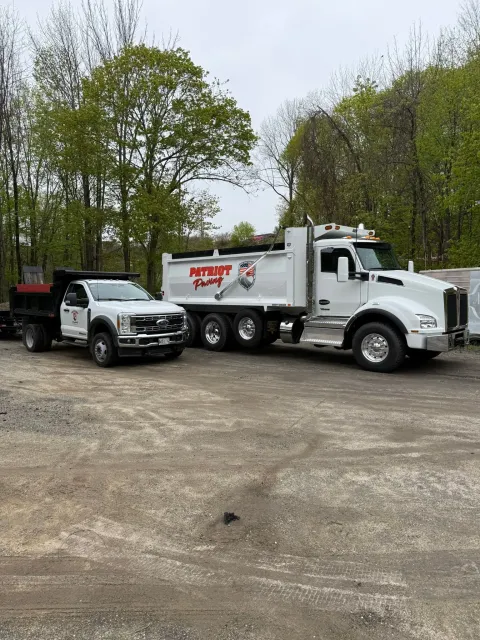 A white pickup truck and a larger white dump truck, both with