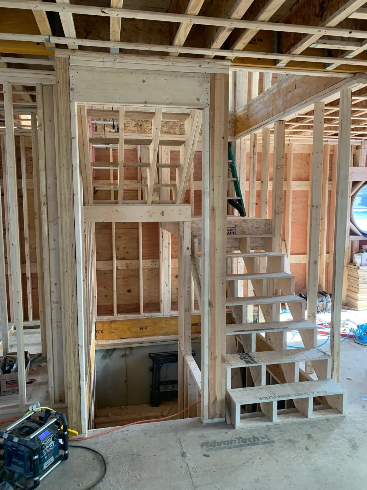 Interior view of a house under construction with wooden framing, stairs, and a small opening above the stairs. Scituate, Norwell, Hanover, Hanson, Marshfield, South Shore. Massachusetts Local Construction Company.