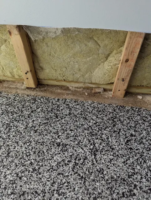 A construction area with insulation material between wooden studs and a speckled black and white floor.
