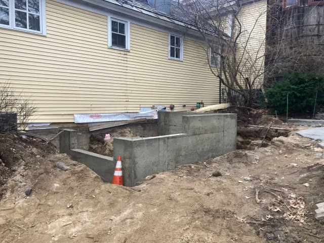 A yellow house with a concrete foundation in front of it.