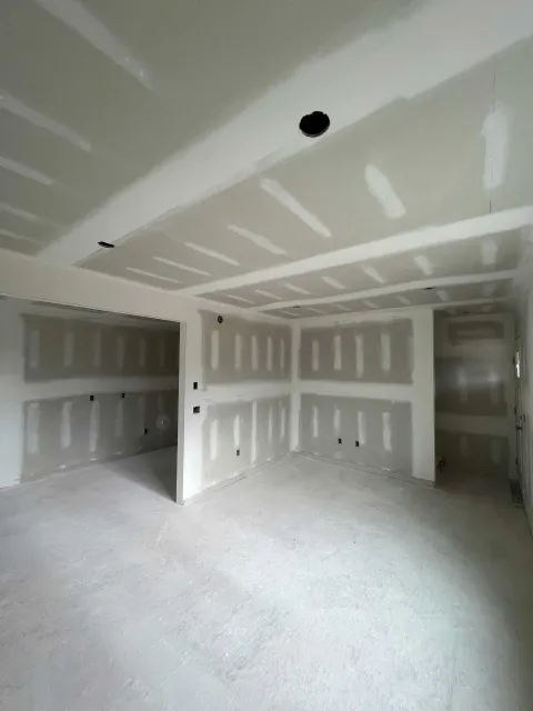 Interior of a room under construction, with drywall on walls and ceiling. Bare concrete floor.