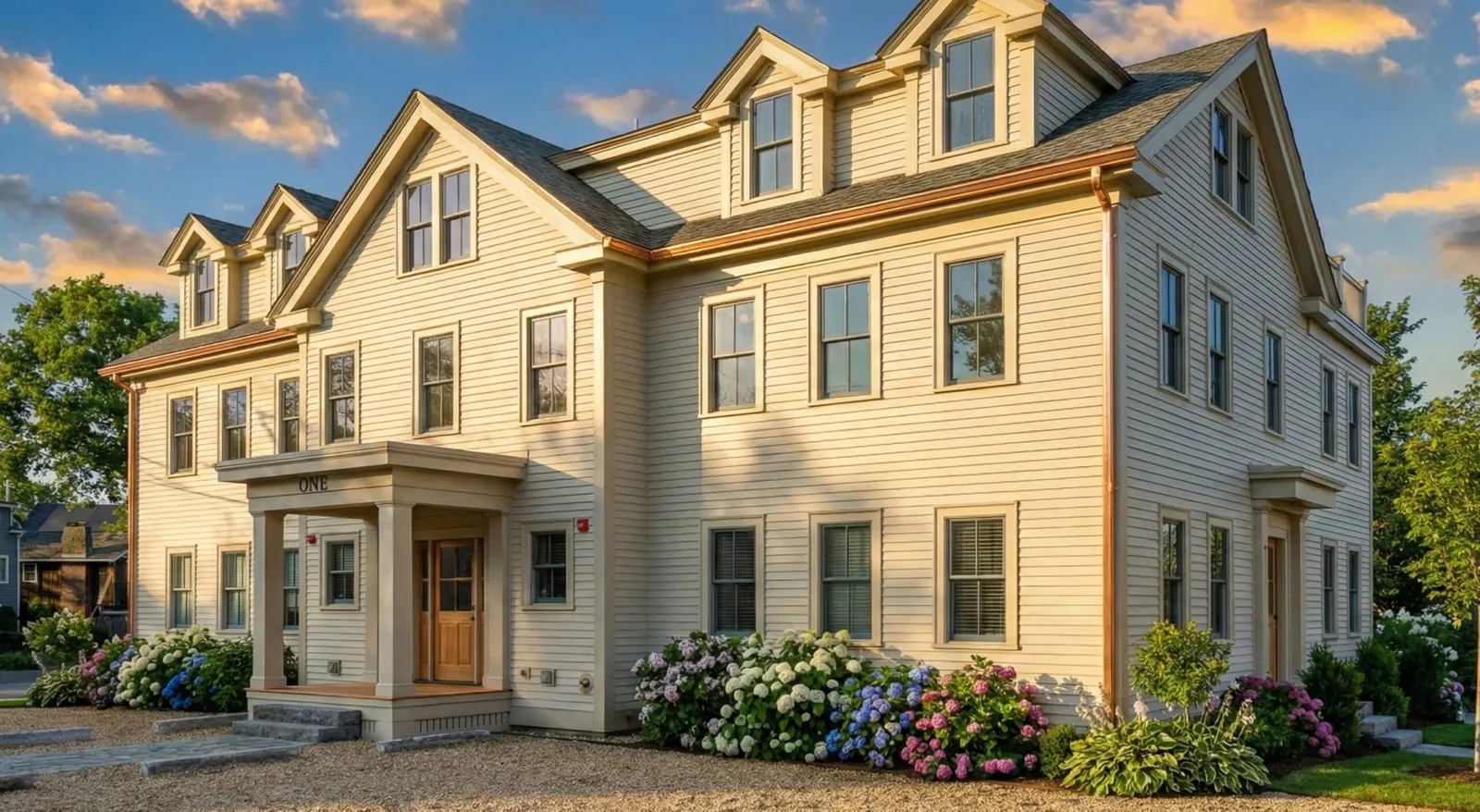A large beige two-story house at 17 Smith Place features multiple windows, dormers, a covered front entrance, and blooming hydrangea bushes in the landscaped garden.