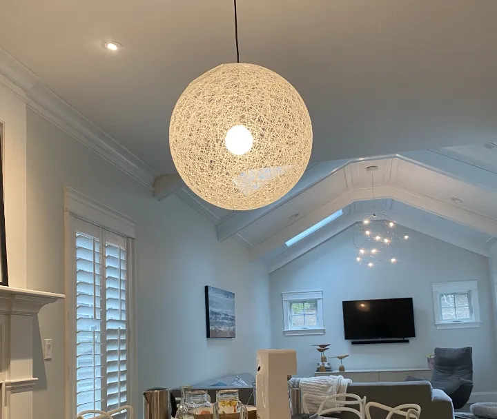 Modern living room with vaulted ceiling, woven pendant light, and white kitchen in background