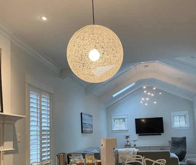 Modern living room with vaulted ceiling, woven pendant light, and white kitchen in background