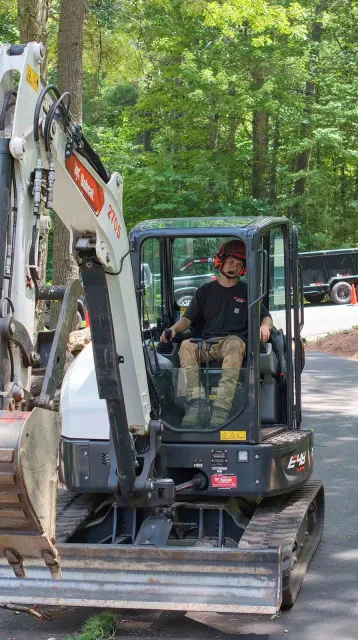 Person operating an excavator on a wooded dirt path.