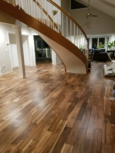 A grand entryway with a curved wooden staircase and rich, multi-tonal walnut-style flooring.