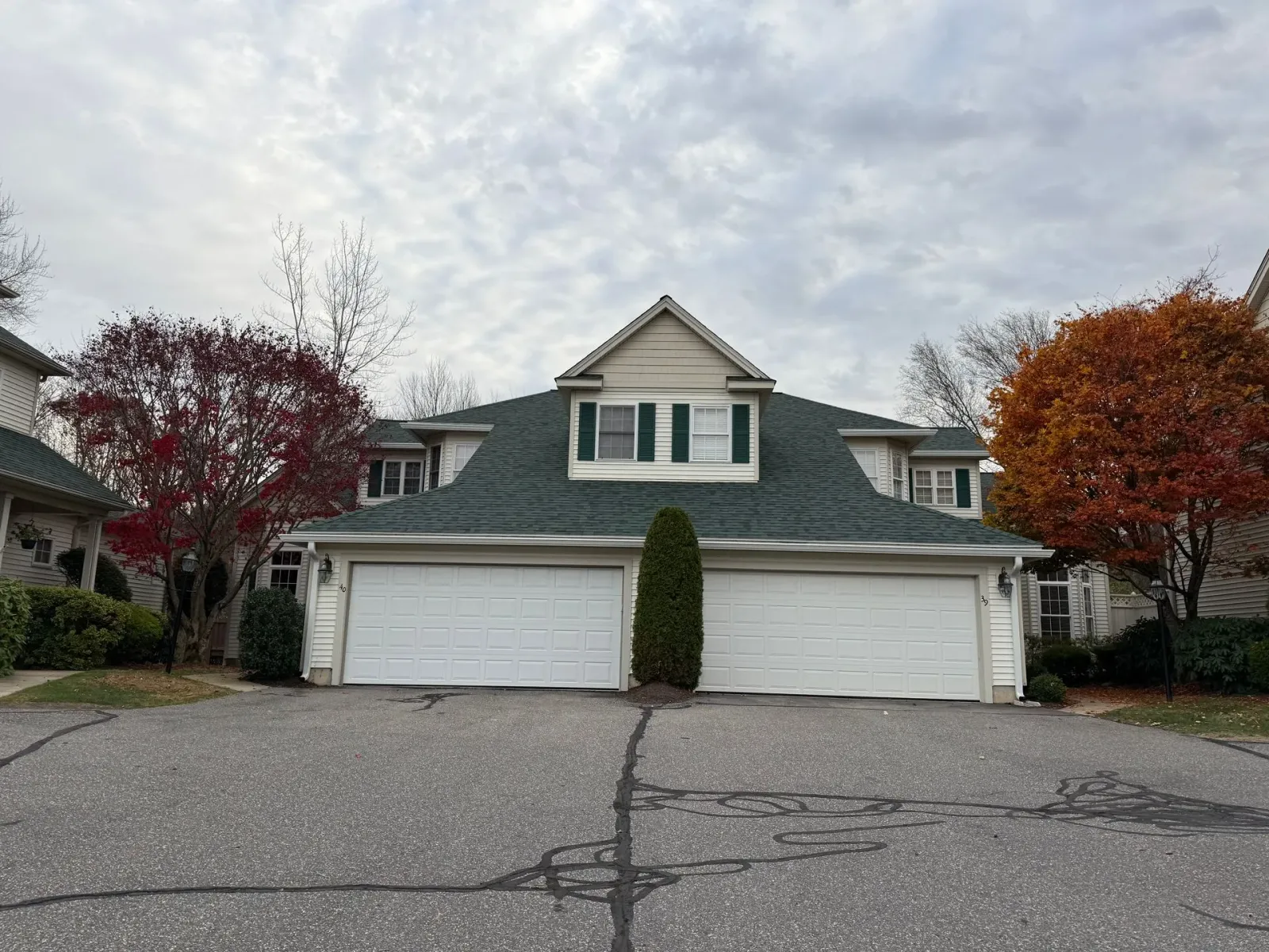 Suburban townhouse with three white garage doors, green roof, and autumn trees under cloudy sky