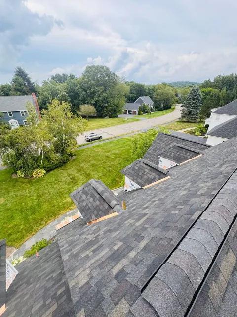 View from a roof over a suburban street, lawns, trees, and cloudy sky