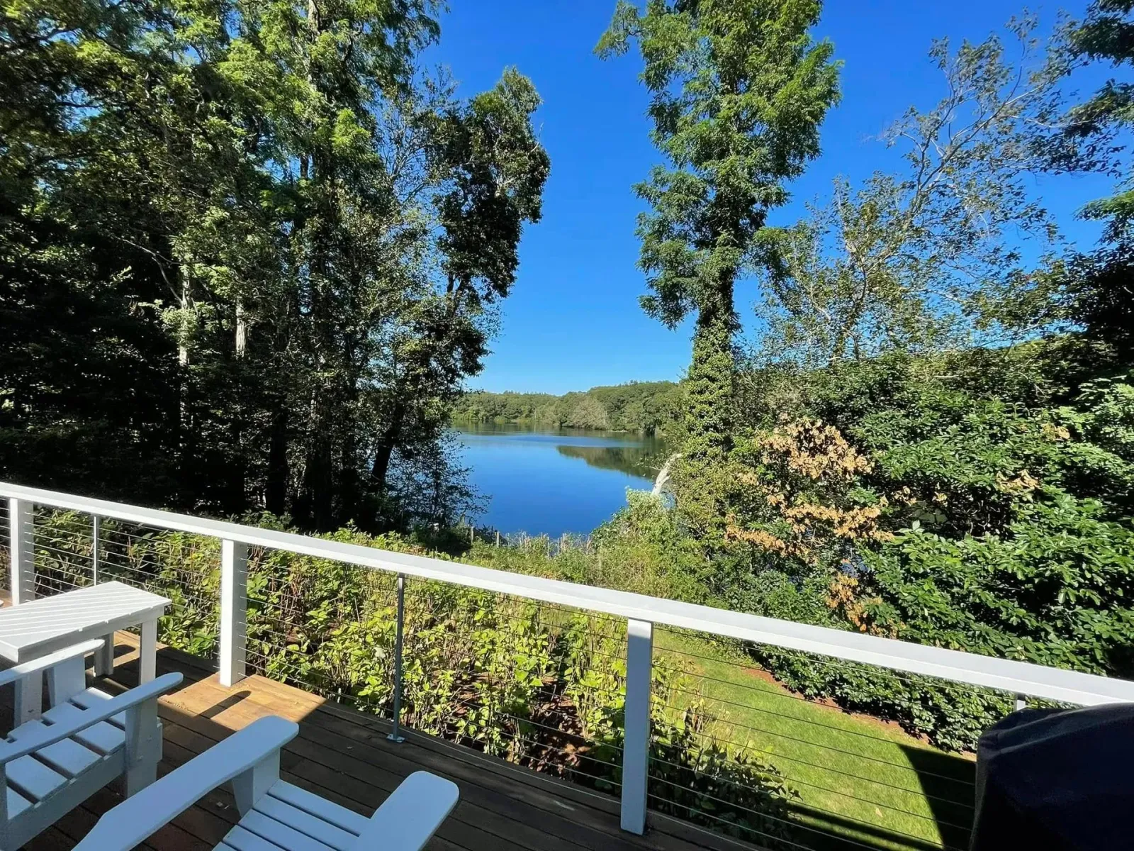 Deck overlooking a calm lake, framed by green trees under a blue sky.