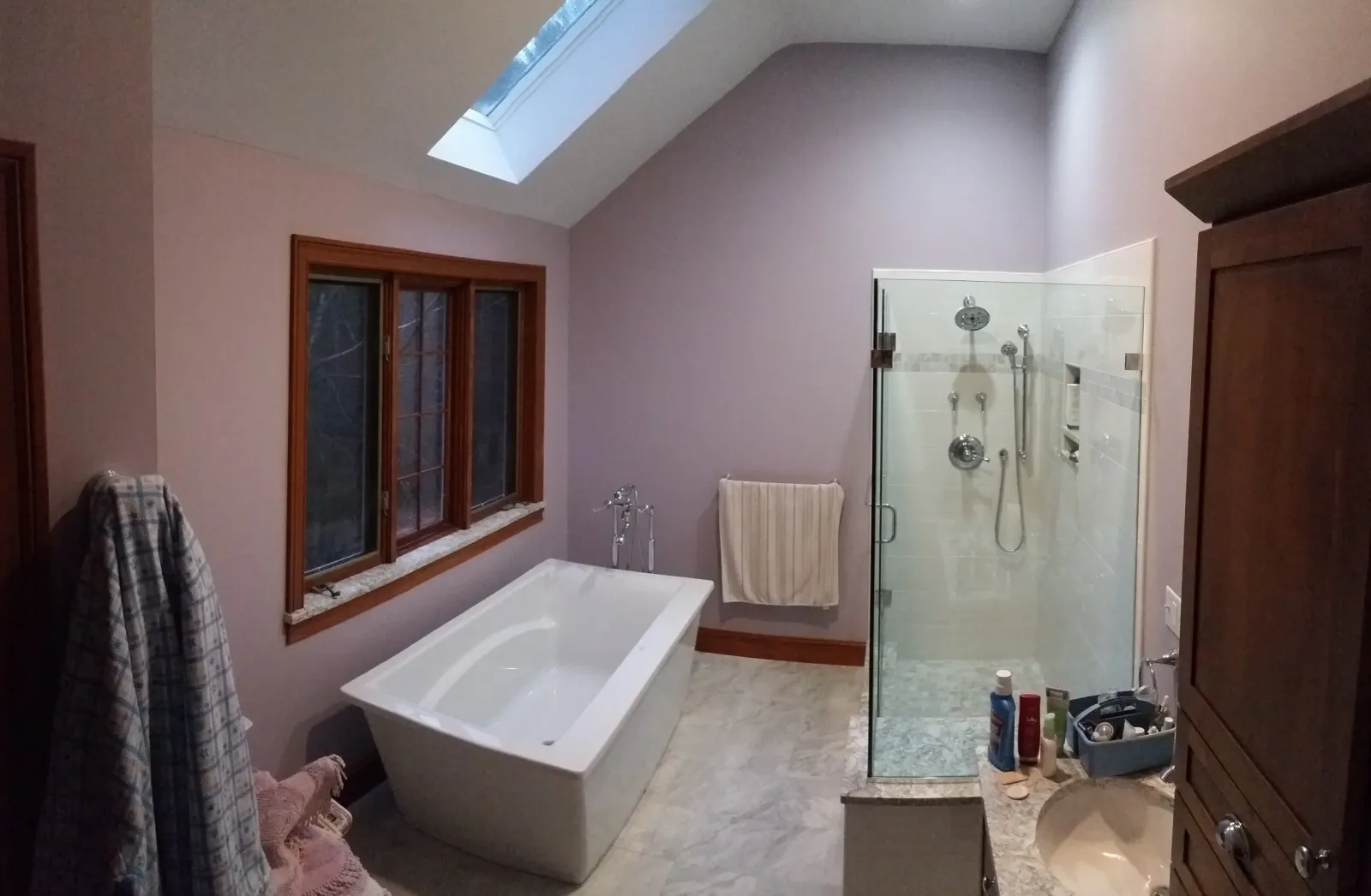 Bathroom with a freestanding bathtub, a glass-enclosed shower, panoramic window, and stained wooden trims.