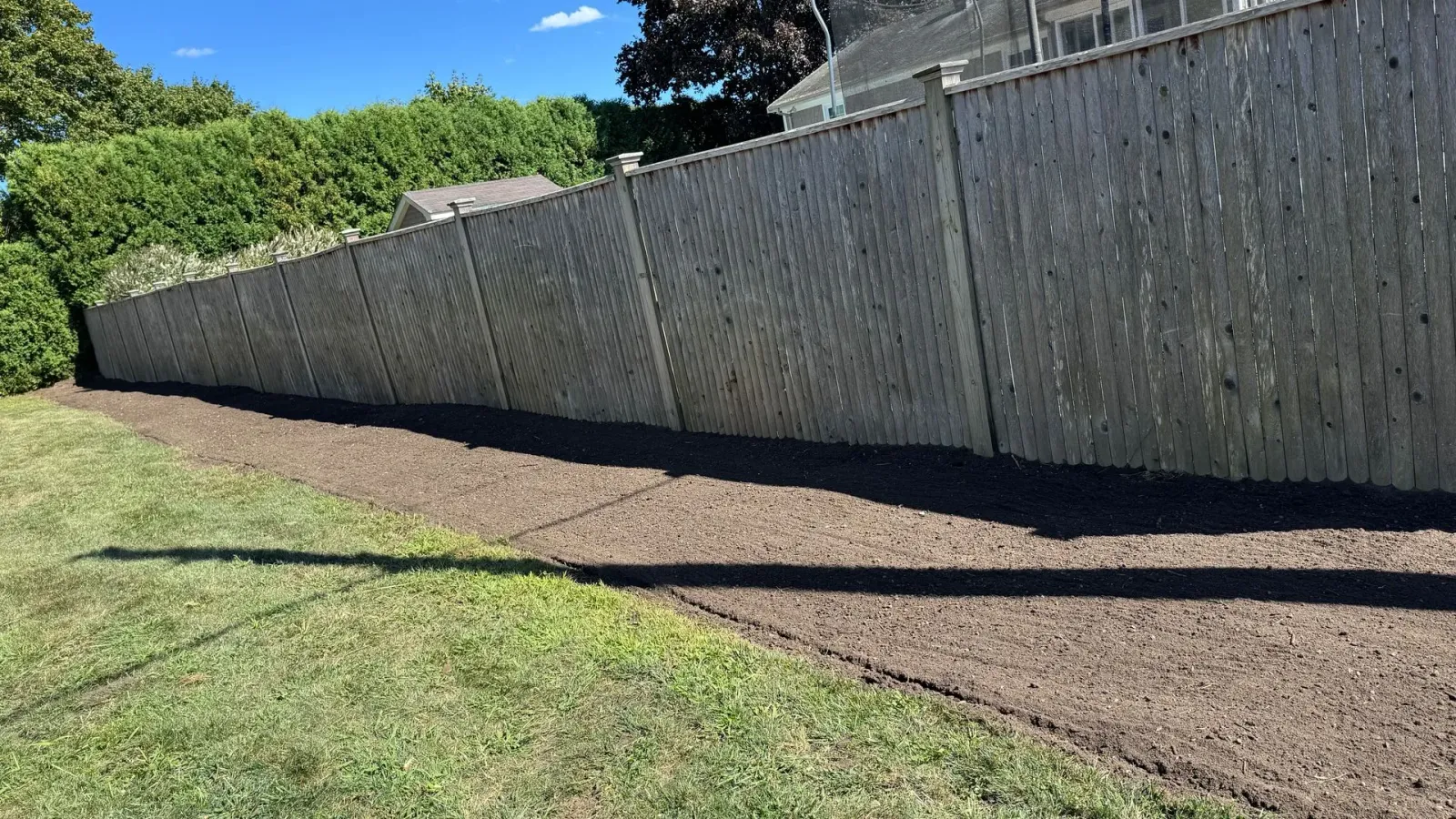 Long wooden fence along a dark mulch bed next to a grassy lawn.
