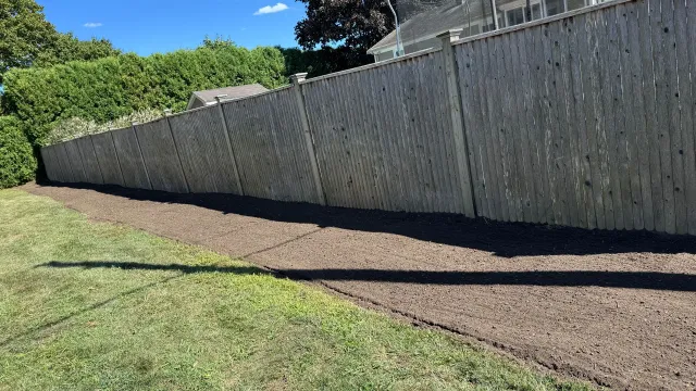 Long wooden fence along a dark mulch bed next to a grassy lawn.