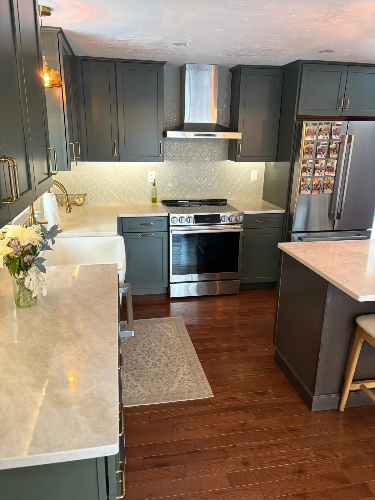 Modern kitchen with dark cabinets, stainless steel stove, white countertops, and a central island on wood floors