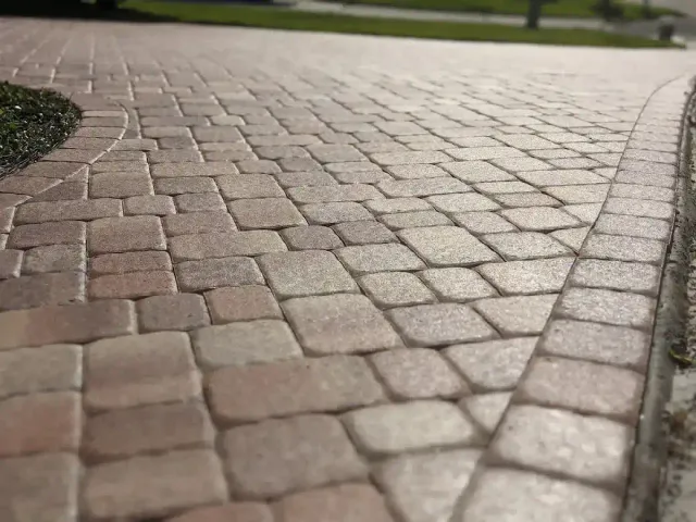 Close-up of a curved driveway paved with interlocking stone bricks in varying shades of light brown and beige.