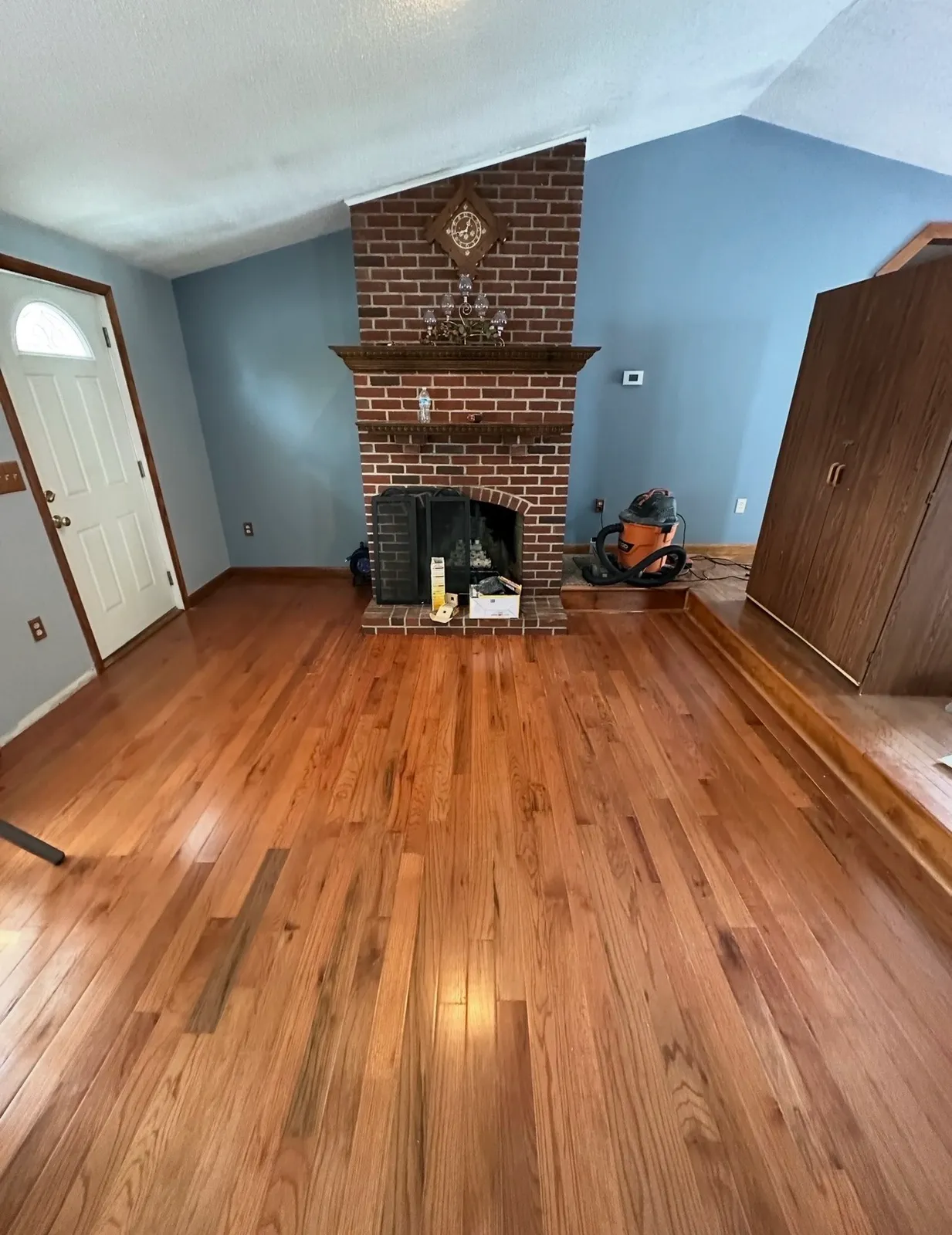 Living room with refinished red oak hardwood floors and original brick fireplace before repainting