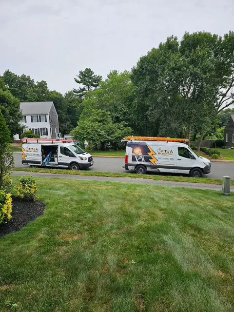 Two white service vans parked on a grassy roadside near trees and a house