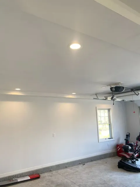 Empty white garage interior with recessed lights, a window, and tools near the right wall