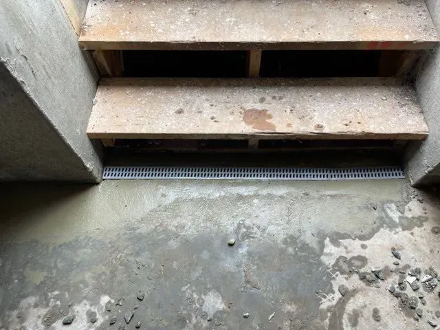 Rusty wooden steps above a stained concrete floor with a drainage grate below
