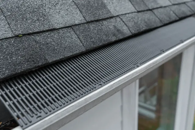 Close-up of a house roof edge with a black gutter guard protecting a metal gutter.