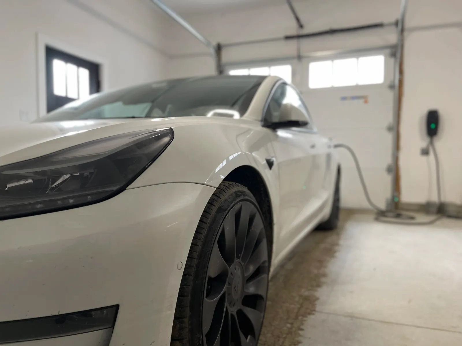 Close up of the front of an electric car that is connected by cable to a charger in the wall of a garage