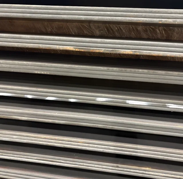 Close-up of stacked metal pipes or rods, varying in color from silver to rusted brown, organized horizontally.