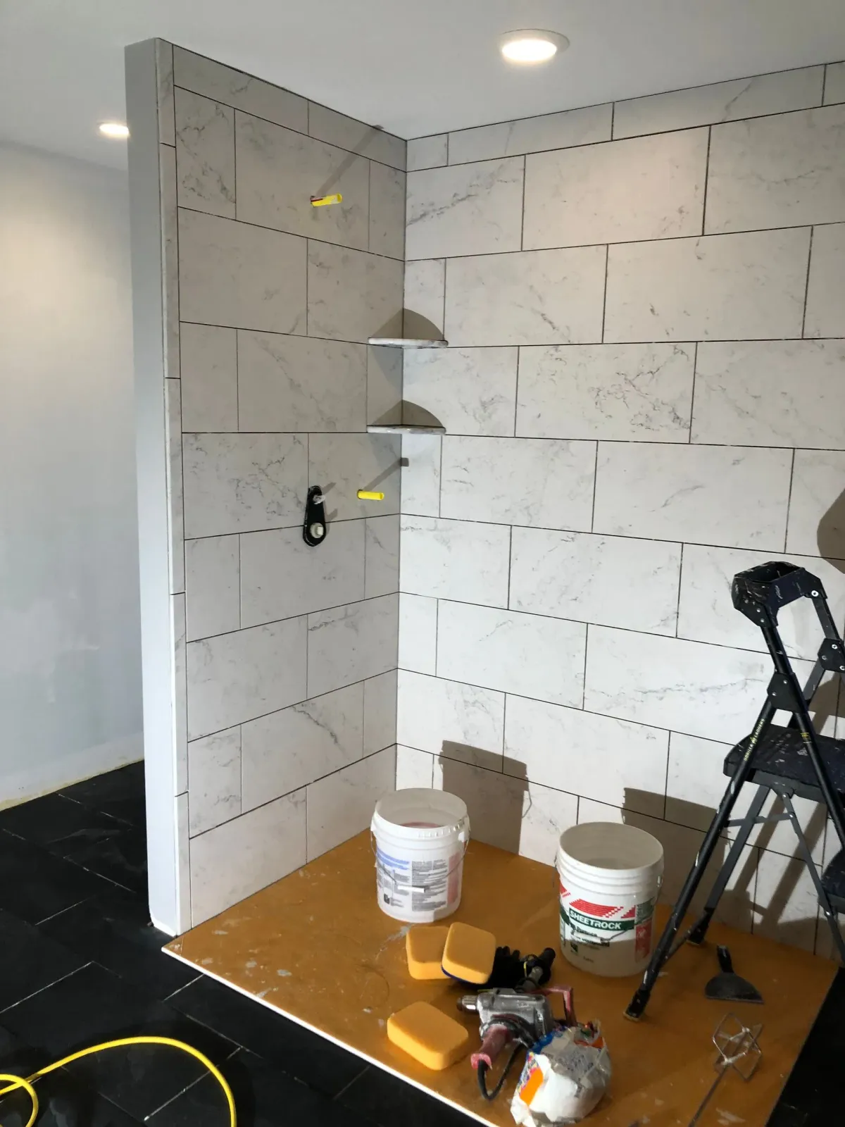 Small room with white wall tiles, paint buckets, tools, and a step ladder during renovation.
