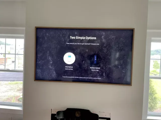 Wall-mounted TV showing “Two Simple Options” in a bright room with windows and a chair below.