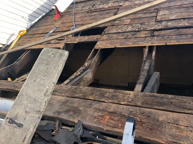 Damaged roof with exposed wooden beams and missing shingles during repairs