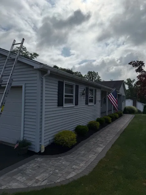 Single-story house with gray siding, American flag, ladder, and cloudy sky