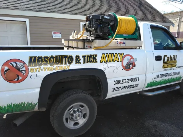 Mosquito and tick control truck with hose reel parked beside a building