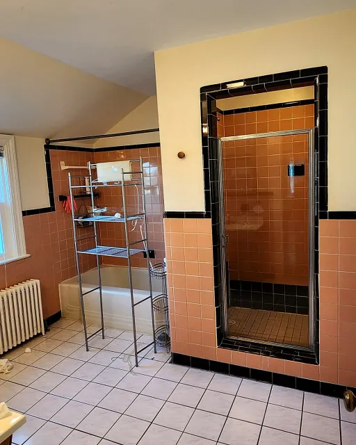 Dated bathroom before remodeling, with salmon wall tile, black trim and an enclosed shower stall