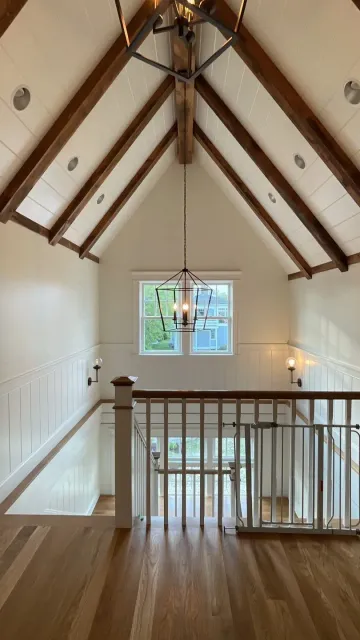 Wooden staircase with a high ceiling featuring exposed beams and a hanging chandelier.