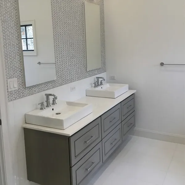 Modern bathroom with gray vanity, white countertops, and dual sinks.