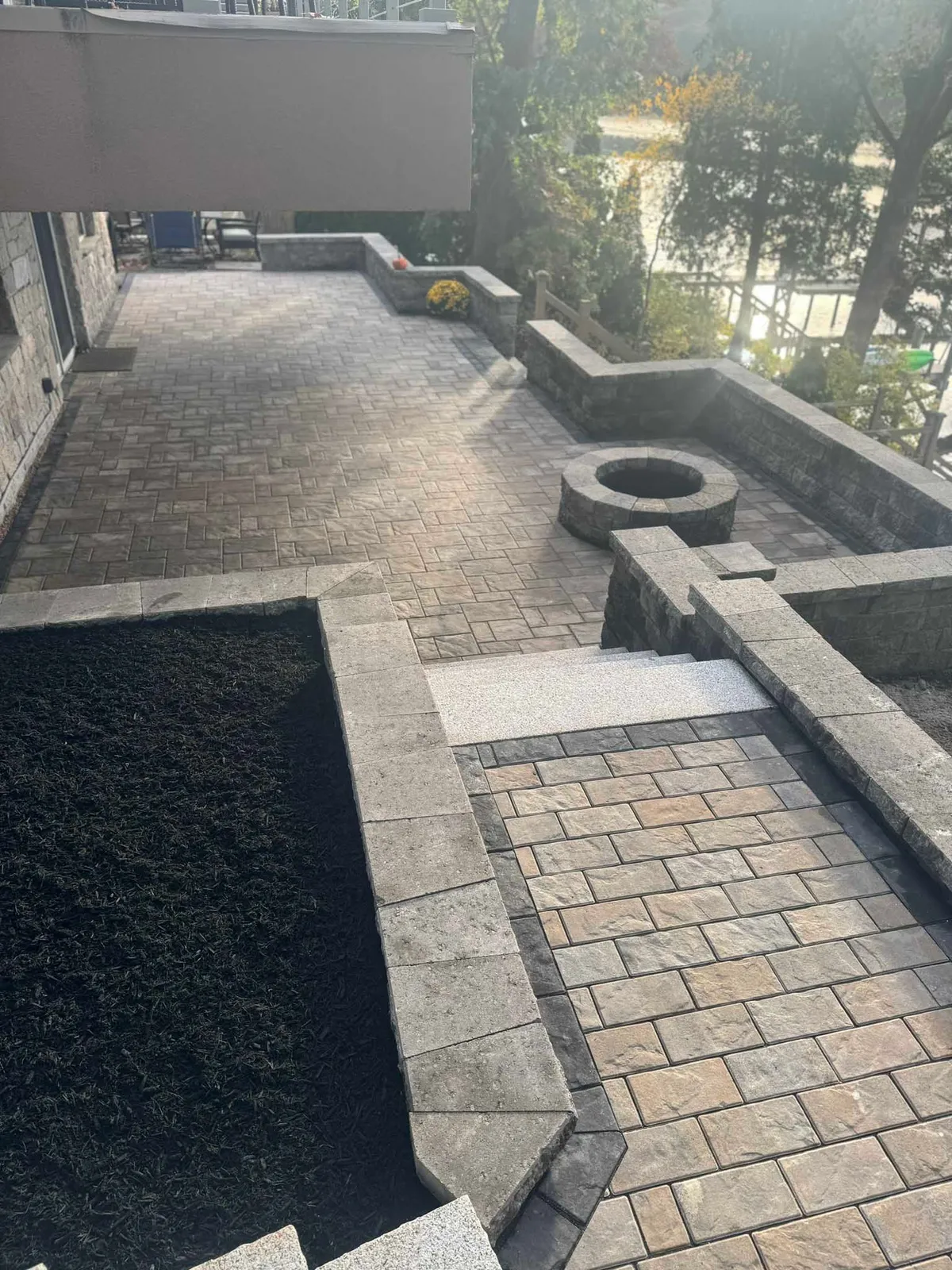A stone patio with a built-in fire pit, stone retaining walls, and a matching walkway leading to a garden area.