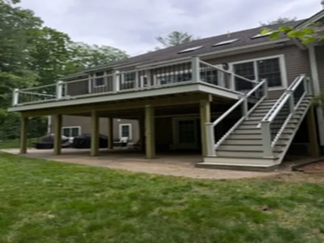 Two-story house with a raised deck, stairs, and covered patio in a grassy yard