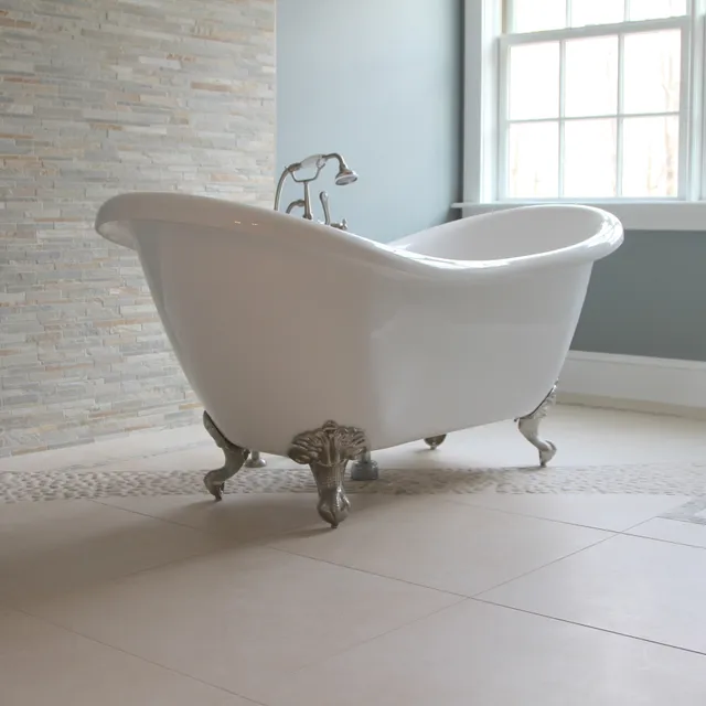 White clawfoot bathtub with silver feet on beige tile floor, stone accent wall, and pebble tile border.