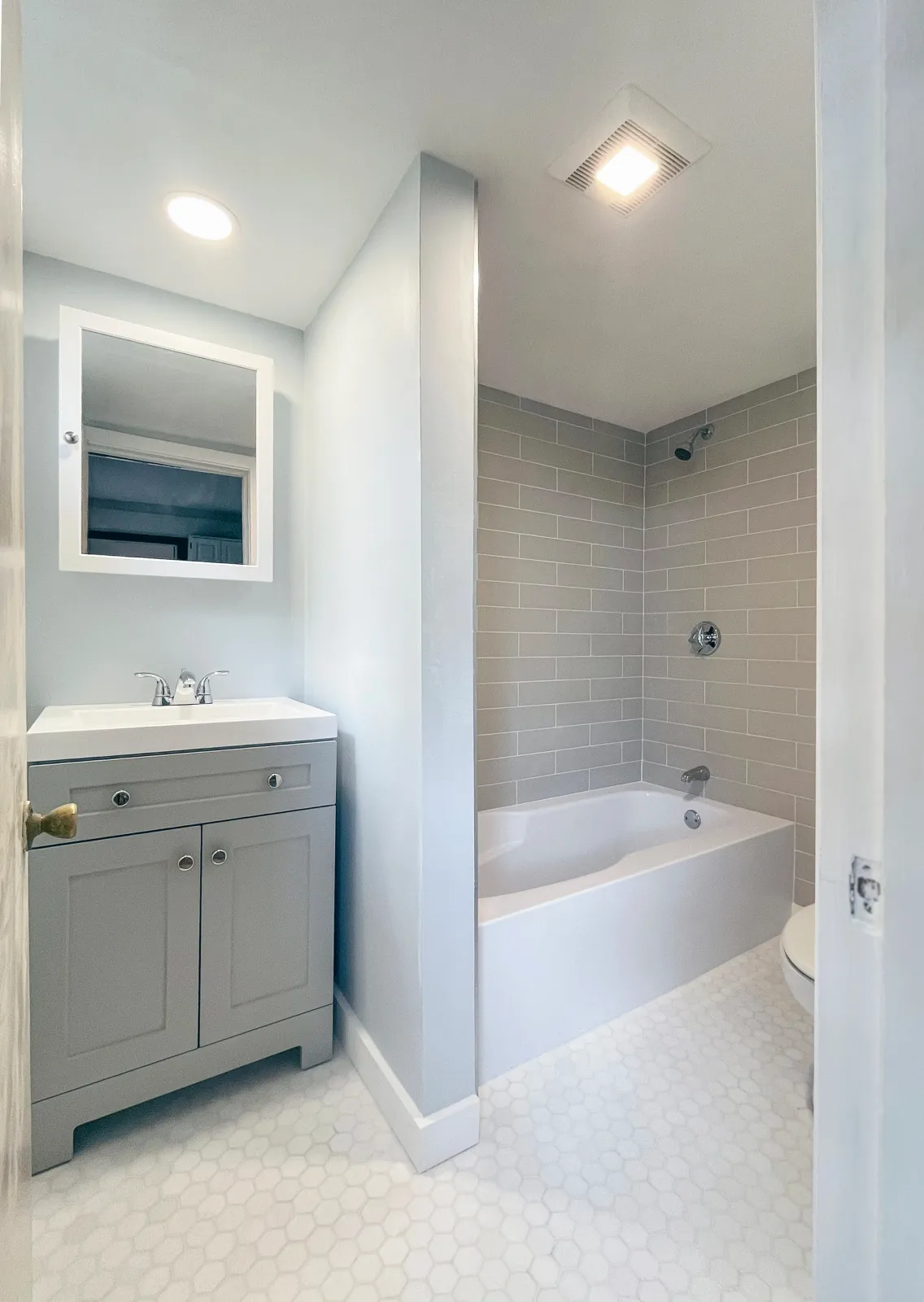 Bathroom with light blue walls, a gray vanity with a mirror above, and a separate shower and bathtub area with beige subway tiles.